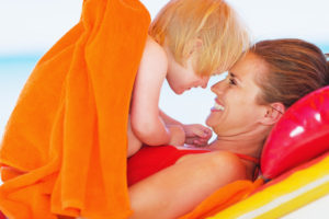 Mom at the pool laying on a raft with her baby in her arms. They are forehead to forehead smiling at each other. She feels better after postpartum therapy in California after searching for a postpartum therapist in San Diego, CA.