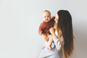 A woman holds her baby looking happy. She is feeling less of her postpartum depression symptoms in San Diego, CA since she started working with Headway Therapy. They have postpartum therapy in California that is effective.