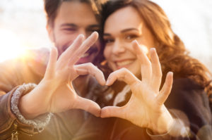 A couple makes a heart with their fingers. They are feeling happy since starting online premarital counseling in California with Headway Therapy.