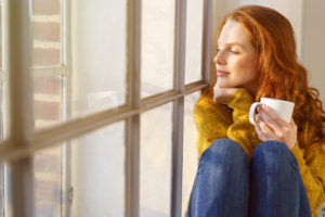 A woman looks out a window. She is feeling happy since starting miscarriage therapy in San Diego, CA. She opted for online miscarriage therapy in California.