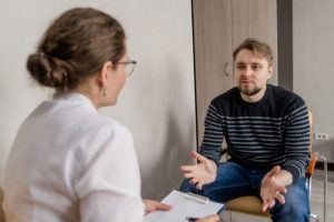 A man sits in with a healthcare provider. This represents concepts of trauma therapy in San Diego, CA.  Headway predominantly provides online therapy for women in California. This often includes online pregnancy counseling in California.